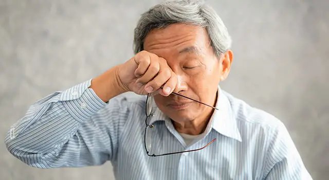 man rubbing eye holding glasses